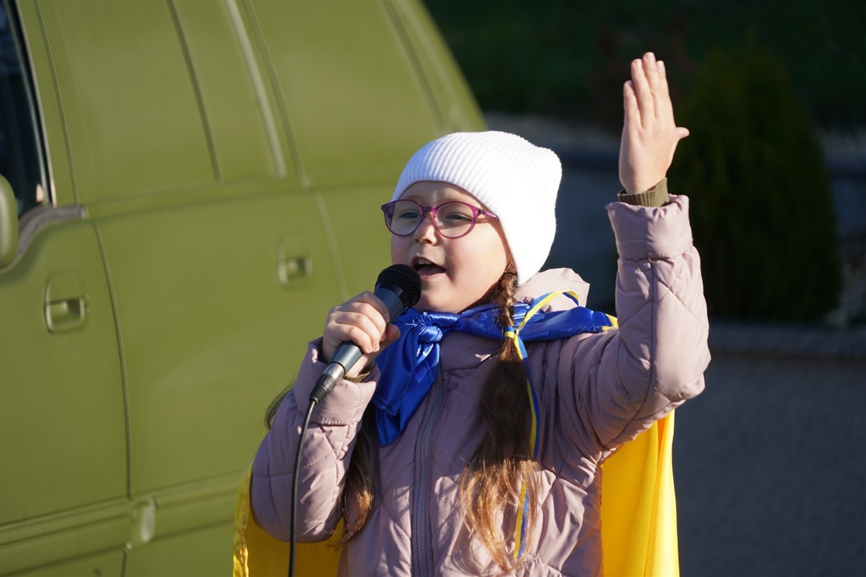 Юна городоччанка співає патріотичну пісню під час передачі автомобілів воїнам